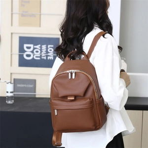 Rear view of a minimalist brown soft leather backpack with a flap buckle and zip pockets