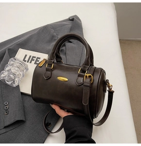 Detail of dark brown Boston bag with golden hardware and cylindrical structure on gray blazer