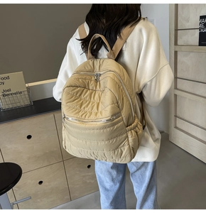 Rear view of model wearing khaki quilted backpack with dual zippers and side pockets
