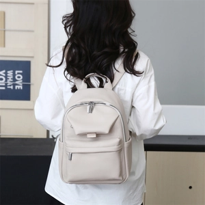 Detail of beige litchi grain leather backpack featuring silver zippers and side pockets