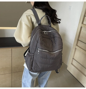 Close-up of quilted padded backpack with metallic zippers and side pockets in taupe brown