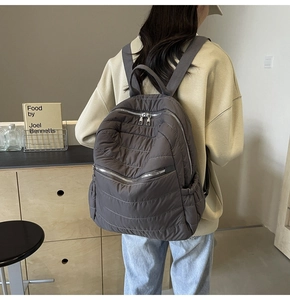 Detail view of quilted grey puffer backpack showing zippers and side storage pockets