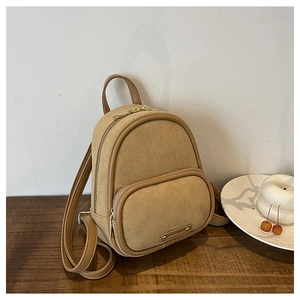 Gros plan du mini sac à dos en daim camel avec bordure en cuir sur bois sombre