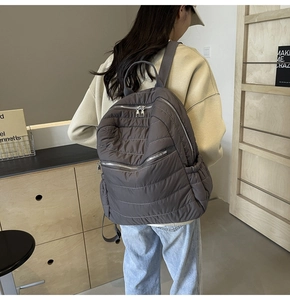 Detailed view of dark taupe quilted backpack with puffer texture and silver zippers