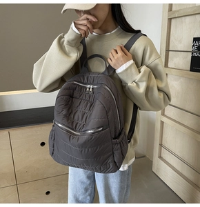Detail of dark taupe quilted nylon backpack showing padded texture and dual zippers