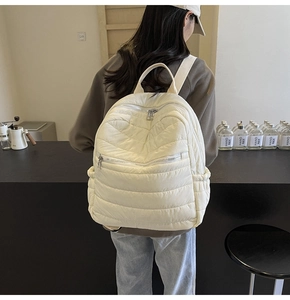 Detailed back view of a woman wearing the quilted beige nylon backpack in a cafe