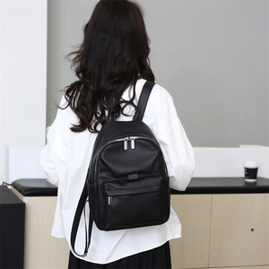 Detail of minimalist black pebbled leather backpack with silver zippers worn on person