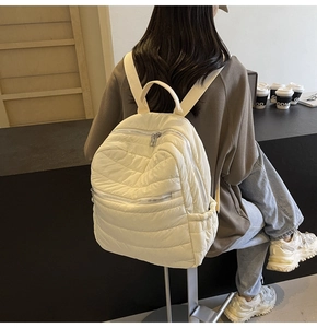 Detailed view of the white quilted backpack showing soft padded fabric and zipper compartments