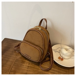 Vue détaillée du mini sac à dos en daim marron montrant la poche avant et le logo doré