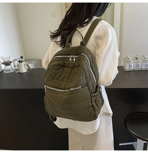 Detail view of olive green quilted backpack with multi-zipper compartments and nylon straps