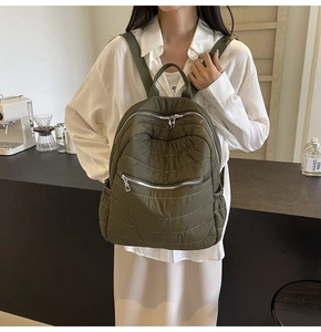 Close-up of olive green quilted backpack featuring silver metallic zippers and padding