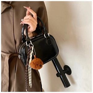 Detail of glossy black handbag with plush bear charm and woven tassel accessory