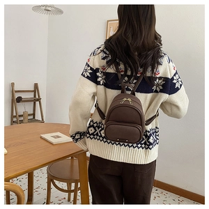 Mannequin portant un mini sac à dos marron avec zips dorés dans un décor intérieur
