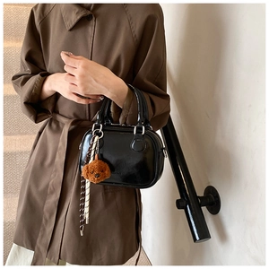 Detail of glossy black leather handbag with cute teddy bear charm and woven rope accent