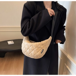 Détail d'un sac bandoulière beige matelassé en demi-lune avec sangle noire sur un mannequin