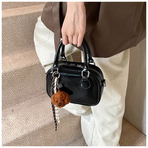 Close-up of black glossy crossbody bag with plush teddy bear charm and striped scarf detail
