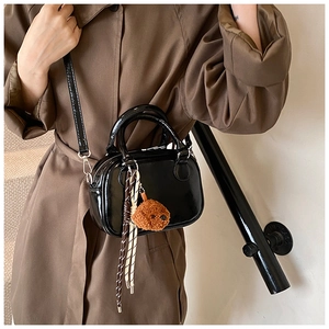 Detail of a shiny black leather bag featuring a cute plush bear charm and woven lanyard