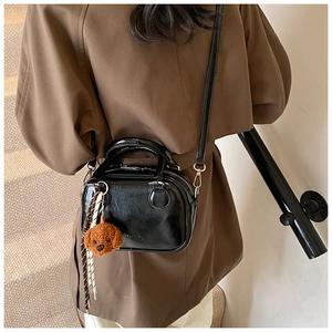 Glossy black mini square bag with cute plush bear charm worn over a camel coat
