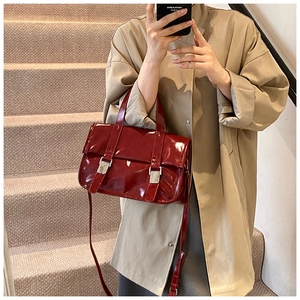 Detail of red patent leather satchel featuring double vertical straps and silver buckles