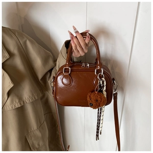 Detail of brown leather handbag featuring a plush teddy bear and woven rope accessory