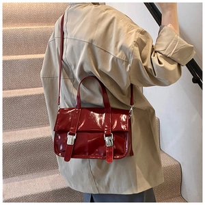 Fashionable dark red glossy patent leather satchel bag held by model on stairs