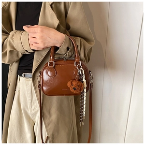 Detail view of brown glossy shoulder bag with teddy bear charm and braided rope accent