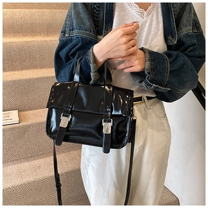 Detail of a vintage black patent leather messenger bag worn on a casual denim outfit