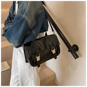 Detail shot of the glossy black messenger bag texture and silver metal buckle accents