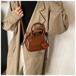 Brown glossy Boston bag detail featuring a cute plush bear charm and sleek leather