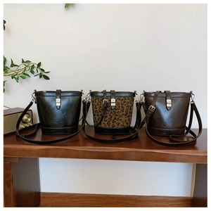 Chic bucket bags in black, leopard print, and brown displayed on a wood bench