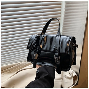 Detail of a black glossy patent leather crossbody bag with vintage buckle straps