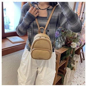 Gros plan du mini sac à dos kaki en daim avec fermetures éclair dorées porté par un mannequin