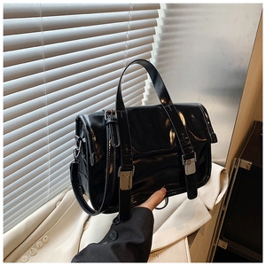 Detail of black glossy patent leather crossbody bag with silver buckles and handle