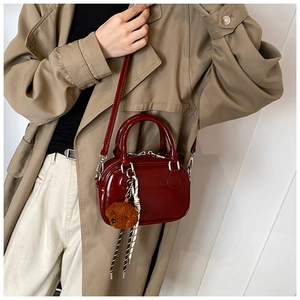 Detail of burgundy patent leather handbag with plush dog pendant on a trench coat