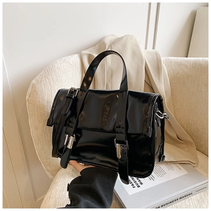 Detail shot of a black glossy patent leather tote bag with decorative buckle and metal clips