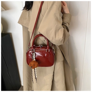 Detail of dark red patent leather square bag with plush dog charm and braided tassel