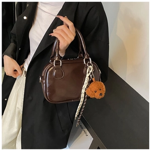 Detail of coffee brown patent leather handbag with plush dog charm and braided strap
