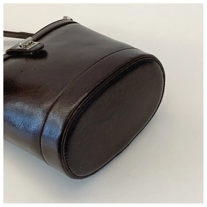 Detailed close-up of dark brown leather bucket bag showing oval bottom and reinforced stitching