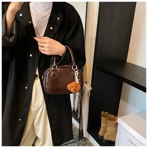 Detail of a dark brown glossy handbag with a cute teddy dog charm in a lifestyle setting