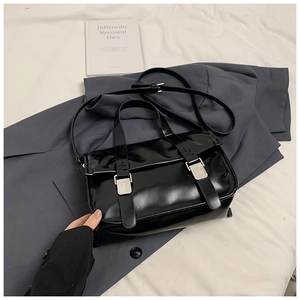 Detail of black glossy messenger bag with dual silver buckles and adjustable strap