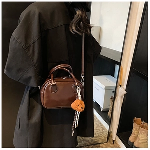 Polished dark brown bowling bag with plush teddy bear charm shown on a model