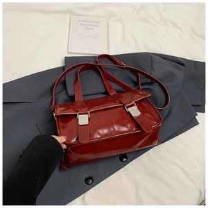 Close-up of dark red glossy shoulder bag with silver buckles on a gray blazer context