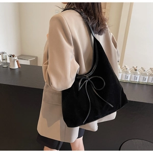 Detail of black suede hobo bag featuring a decorative bow on the shoulder strap