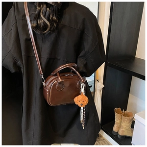 Detail of a dark brown glossy Boston bag with a teddy bear charm on a shoulder strap