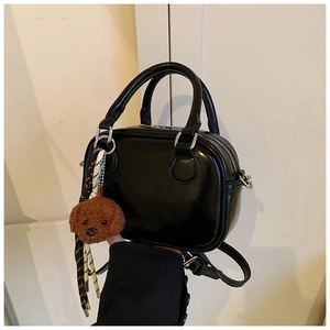 Close-up of black high-gloss mini handbag with a brown poodle plush charm and top handles