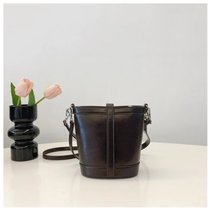 Detailed shot of dark brown glossy bucket bag featuring silver hardware on a white table