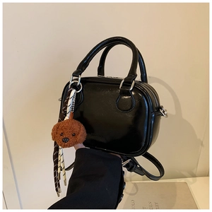 Polished black patent leather bag detail with brown teddy dog charm and woven cord