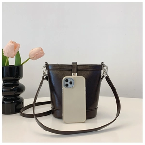 Detail of dark brown bucket bag with shiny faux leather texture next to a smartphone