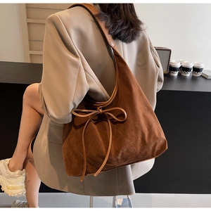 Detail of a brown suede shoulder bag with a bow accent worn with a beige blazer