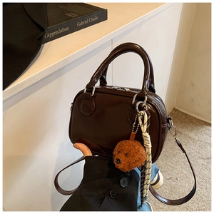 Detail of dark brown glossy leather handbag with bear charm and woven strap on display